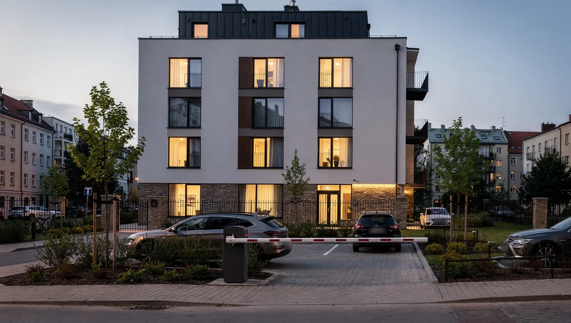Aparthotel o zmierzchu z parkingiem dla gości i szlabanem na wjeździe.